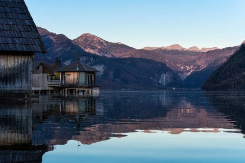 Lake Grundlsee in autumn at sunset. Boathouses on the left, mountains in the background. Blue sky,