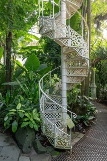 Decorative white cast iron spiral staircase amidst lush vegetation, historic greenhouse, palm