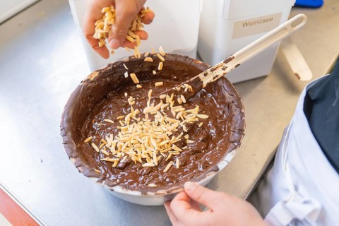 Almonds are added to a dark chocolate mixture in a bowl, Production Burch Schokolade, Haselstaller