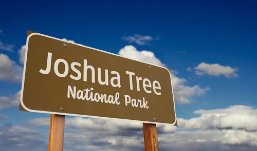 Joshua tree national park (california) road sign against blue sky and clouds