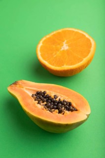 Ripe cut papaya and orange on green pastel background. Side view, close up. Tropical, healthy food,