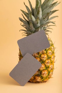 Gray paper business card with ripe pineapple on orange pastel background. Side view, copy space.