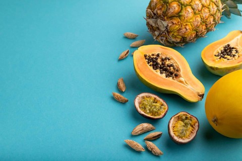 Ripe cut papaya, pineapple, melon, passion fruit, almonds on blue pastel background. Side view,