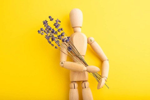 Wooden mannequin holding lavender flowers on yellow pastel background. copy space, isolated,