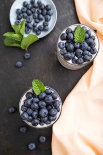 Yogurt with blueberry and chia in glass on black concrete background and orange linen textile. top