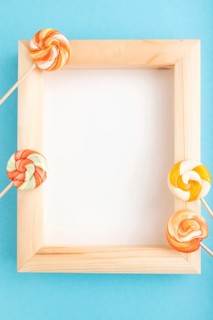 Composition with lollipops and wooden frame on blue pastel background. copy space, top view, flat