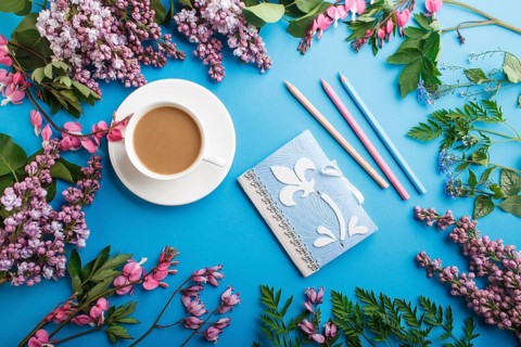 Purple lilac and bleeding heart flowers and a cup of coffee with notebook and colored pencils on
