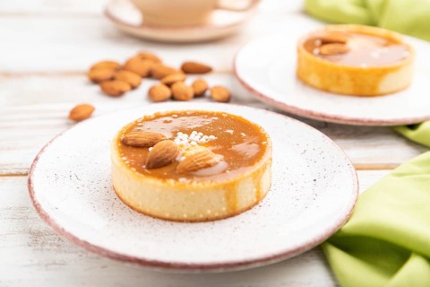 Sweet tartlets with almonds and caramel cream with cup of coffee on a white wooden background and