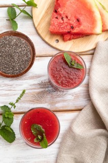 Watermelon juice with chia seeds and mint in glass on a white wooden background with linen textile.