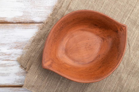 Empty clay brown bowl on white wooden background and linen textile. Top view, close up, flat lay