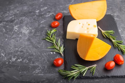 Various types of cheese with rosemary and tomatoes on black slate board on a black concrete
