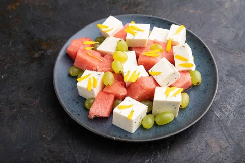 Vegetarian salad with watermelon, feta cheese, and grapes on blue ceramic plate on black concrete