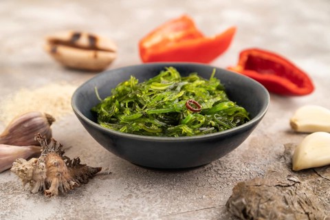 Chuka seaweed salad in blue ceramic bowl on brown concrete background. Side view, close up,
