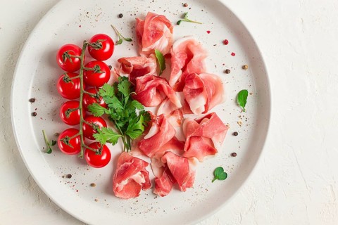 Sliced prosciutto, appetizer, with cherry tomatoes, on a white plate, top view