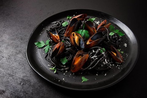Spaghetti with black squid, black pasta, with boiled mussels, on a black plate, with parsley and