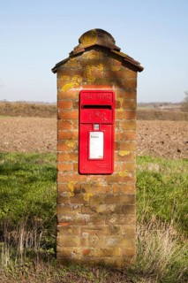 Scarlet red Post Office pillar box mounted in brick with fields in background, Hoo, Suffolk,