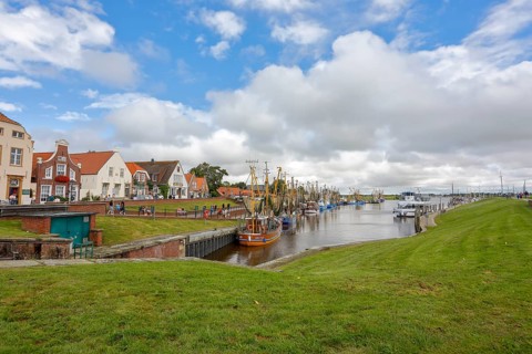 View of historic houses with colourful facades at the old harbour of Greetsiel, with fishing boat,