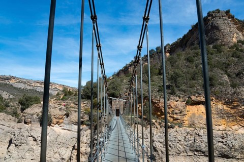 A suspension bridge leads through a rocky gorge with steep walls and green vegetation, Noguera