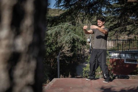 Distant view of a focused man practicing Chi Kung with his eyes closed in the Tree Hugging posture