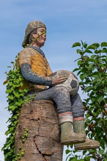 Sculpture of a boy with a football sitting on a tree trunk, Burgstemmen, Lower Saxony, Germany,