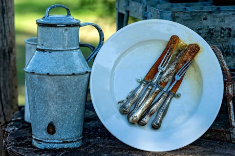Curious rustic still life, rusty cutlery, old milk can made of enamelled tin, decoration in front