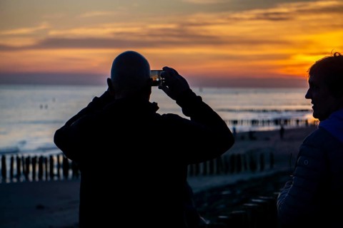 Sunset on the beach of Zoutelande, beach with wooden pile breakwaters, tourists, Zeeland,
