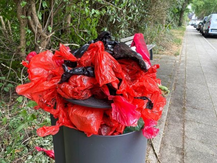 Overflowing rubbish bin, with lots of rubbish, overfilled with dog faeces bags, on a wall path in
