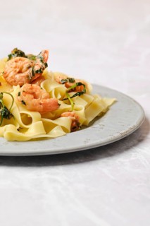 A serving of shrimp fettuccine garnished with fresh herbs is elegantly presented on a gray plate,