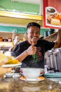 Vendor at a food stall shows thumbs up, looks into the camera, Mercado Central de San José, San