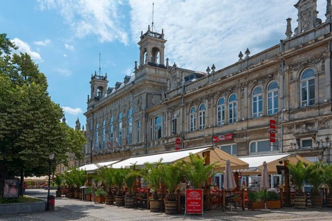 A street café in front of a historic building on a sunny day with blue sky and clouds, Drama