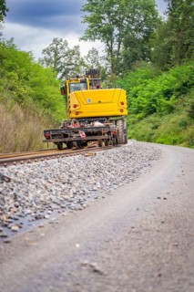 Yellow machine on rails and ballast with trees in the background, track construction, Hermann