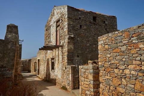 Old stone buildings in an abandoned village under clear skies with visible ruins, Venetian sea
