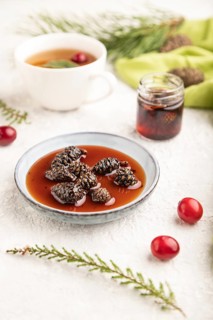 Pine cone jam with herbal tea on gray concrete background and green linen textile. Side view,