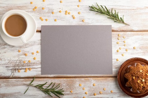Gray paper sheet mockup with cup of coffee and cake on white wooden background. Blank, top view,