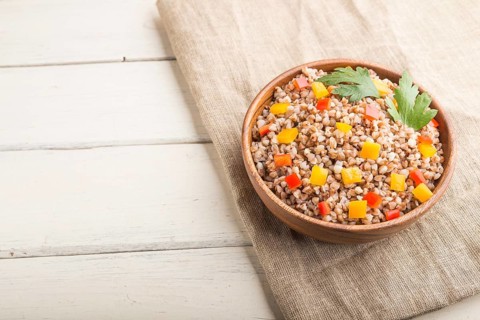 Buckwheat porridge with vegetables in wooden bowl on a white wooden background and linen textile.