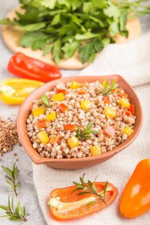Buckwheat porridge with vegetables in clay bowl on a gray concrete background and linen textile.