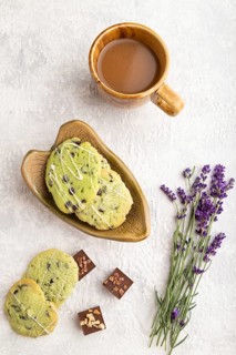 Green cookies with chocolate and mint on leaflike ceramic plate with cup of coffee on gray concrete