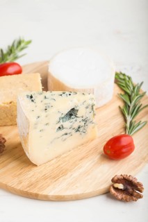Blue cheese and various types of cheese with rosemary and tomatoes on wooden board on a white