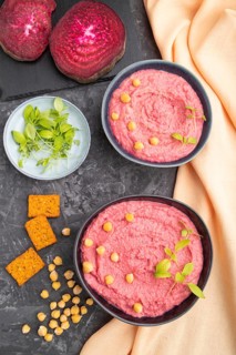 Hummus with beet and microgreen basil sprouts in ceramic bowl on a black concrete background and