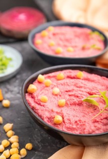Hummus with beet and microgreen basil sprouts in ceramic bowl on a black concrete background and