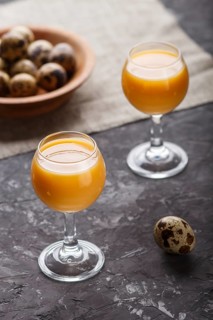 Sweet egg liqueur in glass with quail eggs on a black concrete background. Side view, low key,