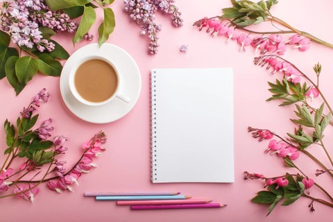 Purple lilac and bleeding heart flowers and a cup of coffee with notebook and colored pencils on