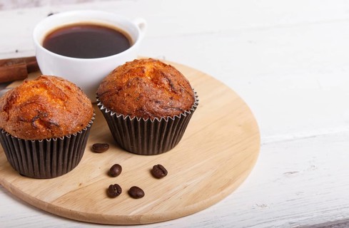 Two carrot muffins with cup of coffee on wooden kitchen board on white wooden background with