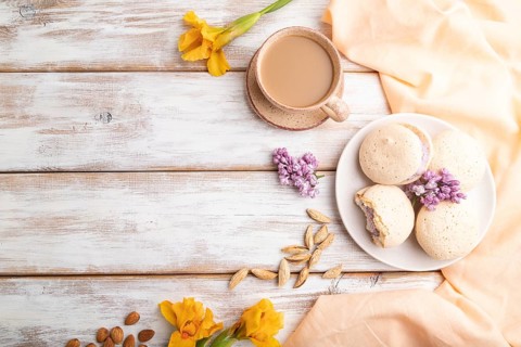 Meringues cakes with cup of coffee on a white wooden background and orange linen textile. Top view,