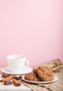 Homemade oatmeal cookies with a cup of cocoa on a linen textile and pink pastel background. side