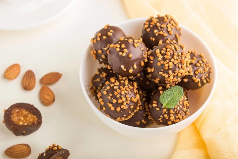 Chocolate caramel ball candies with almonds and a cup of coffee on a white wooden background and