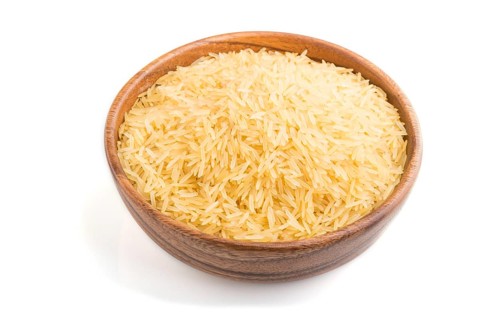 Wooden bowl with raw golden rice isolated on white background. Side view, close up