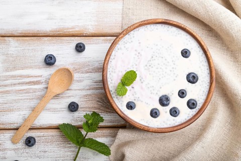 Yogurt with blueberry in wooden bowl on white wooden background and linen textile. top view, flat