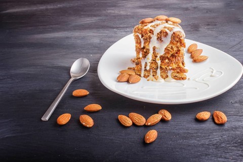 Pie with caramel, white milk sauce and almonds on a white plate on a black wooden background. close