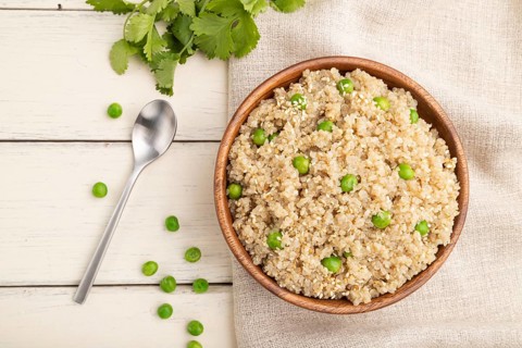 Quinoa porridge with green pea in wooden bowl on a white wooden background and linen textile. Top
